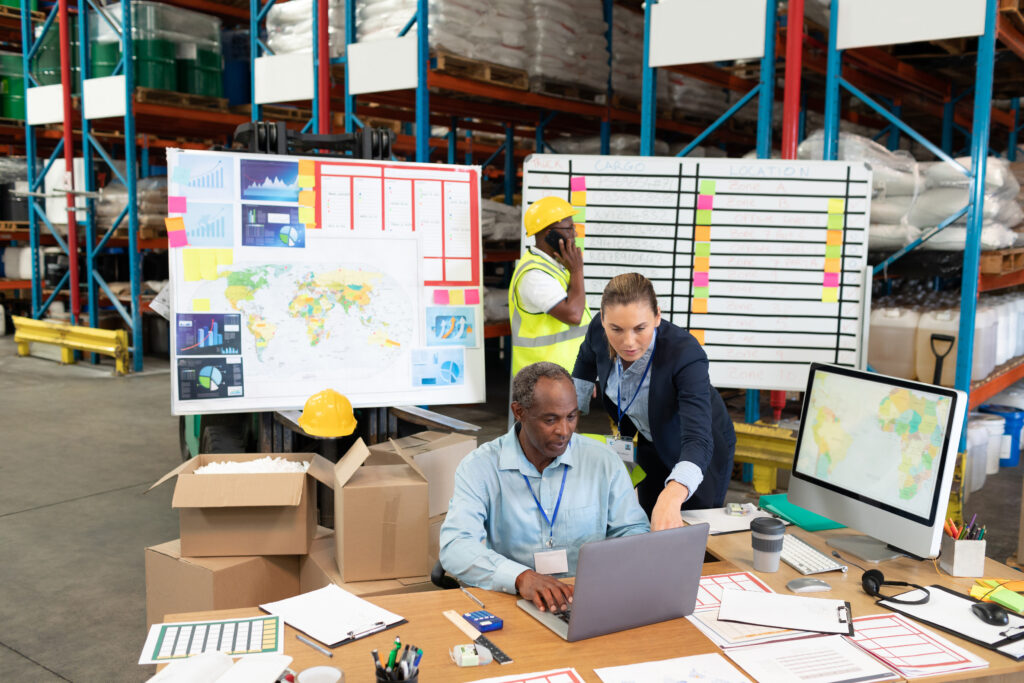 front view of mature caucasian female manager and african american male supervisor discussing over laptop at desk in warehouse. this is a freight transportation and distribution warehouse. industrial and industrial workers concept