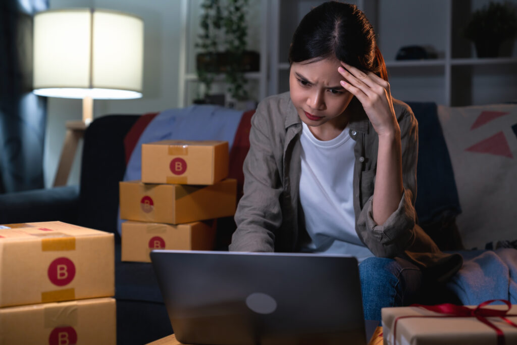 startup small business concept, young woman owner hands touch on the forehead have a headache because of stress, and checking online order on digital laptop with packing on the box at home office.