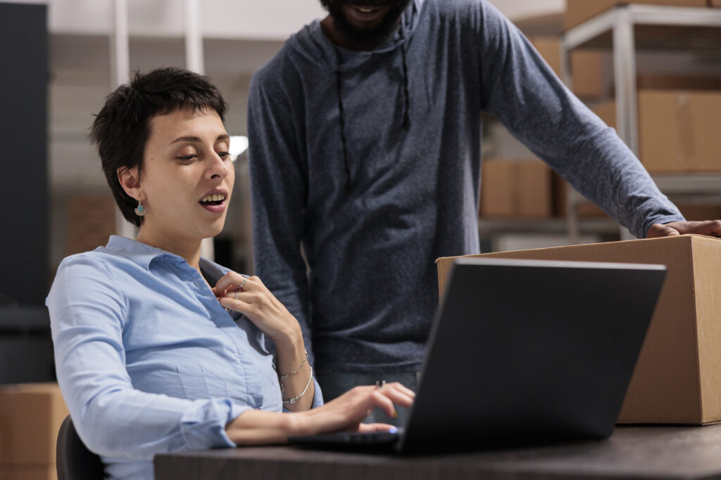 warehouse employees looking at transportation logistics on laptop computer discussing cargo stock