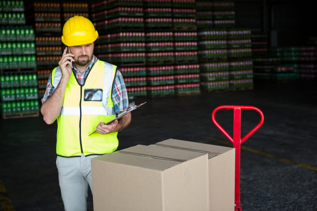 young male worker holding clipboard while talking on phone in factory