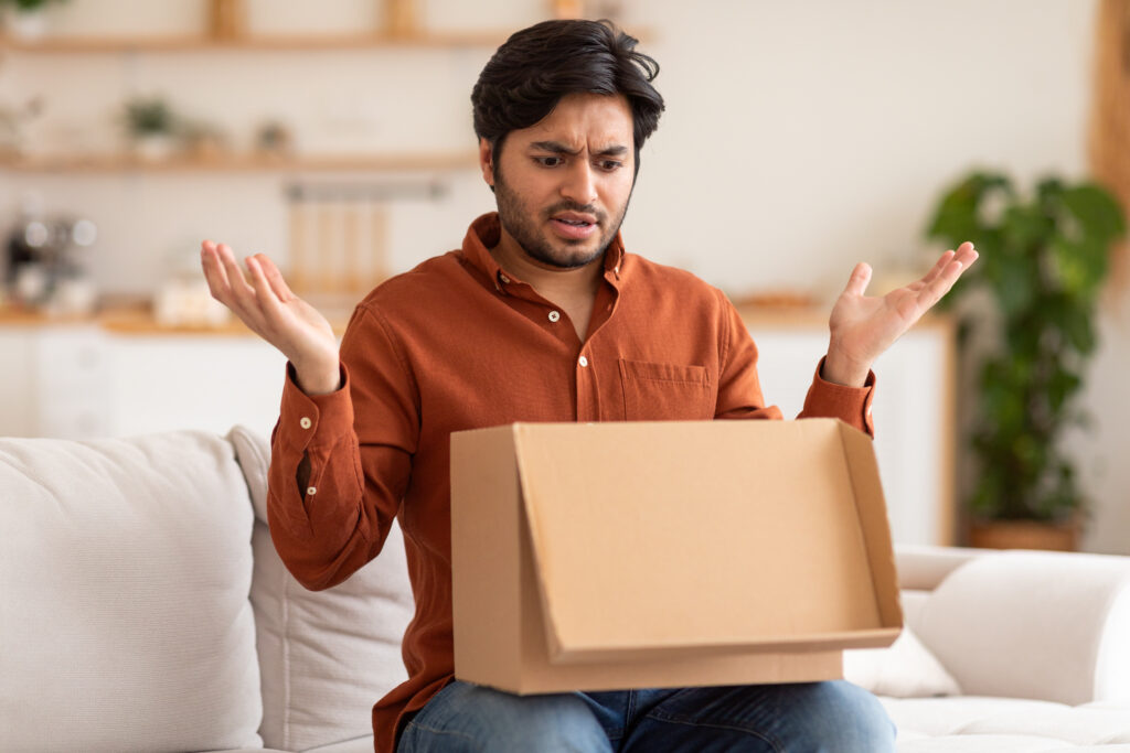 disappointed man opening cardboard box in living room