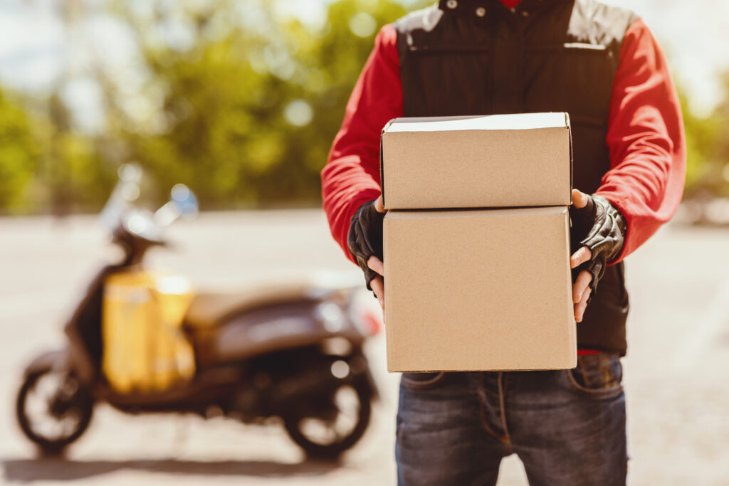 unrecognizable courier delivering parcels offering boxes to camera in city